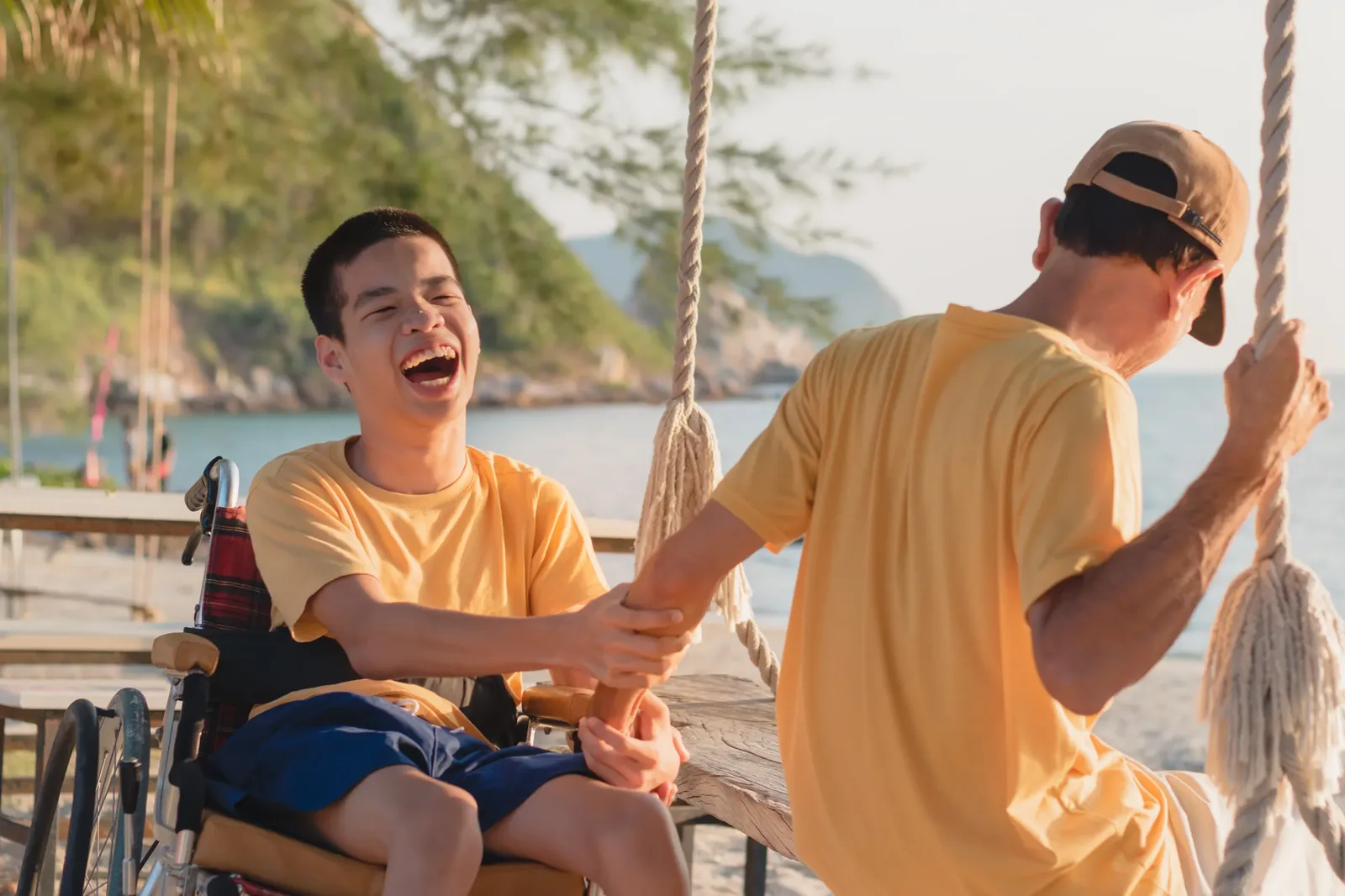 Young man in wheelchair laughing with friend at beach